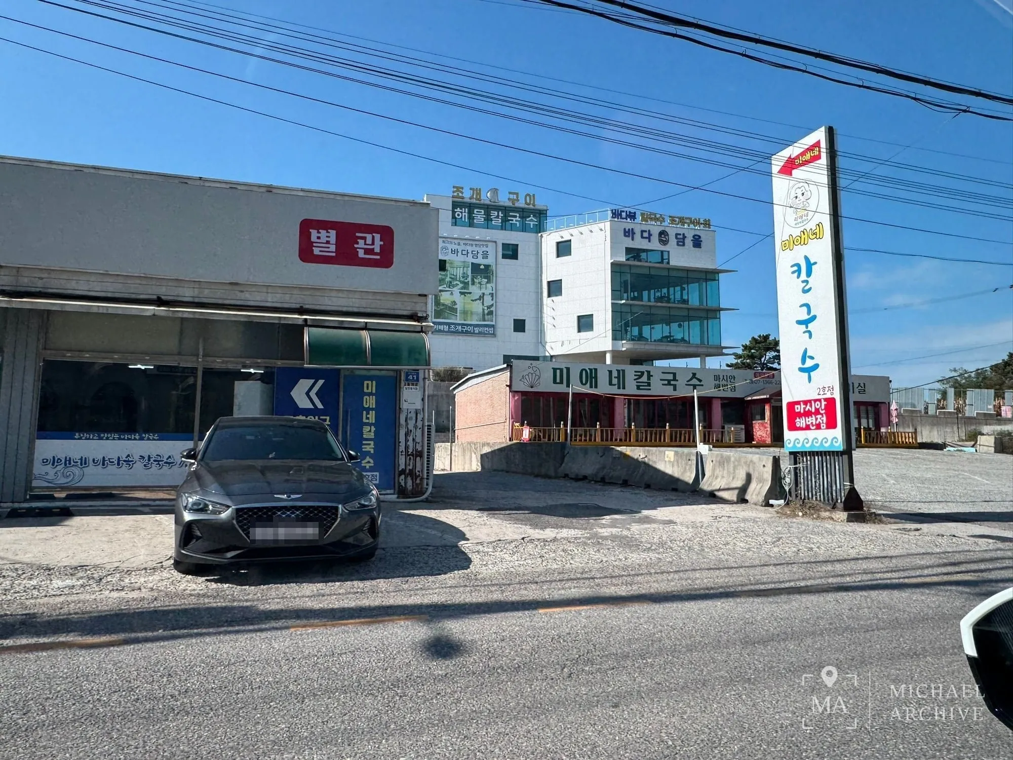 왼쪽에 「별관」 간판이 붙은 건물, 오른쪽 길가에 「미애네 칼국수 · 2호점 · 마시안해변점」 세로 간판. 그 사이로 주차장 쪽 길이 나 있다