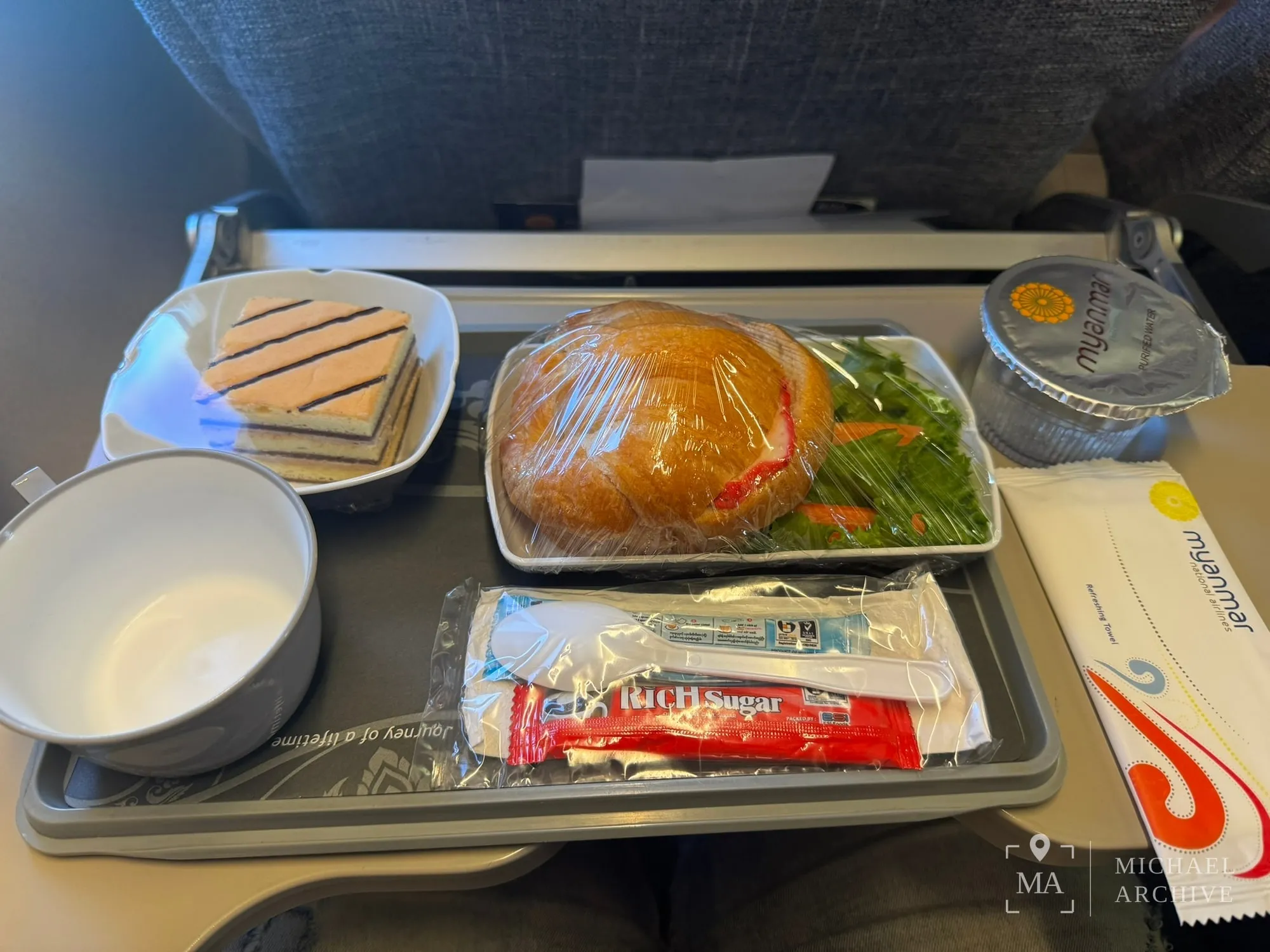 기내 트레이. 빵과 채소, 조각 케이크, 물컵, 설탕과 커피 스틱이 담겨 있다.
