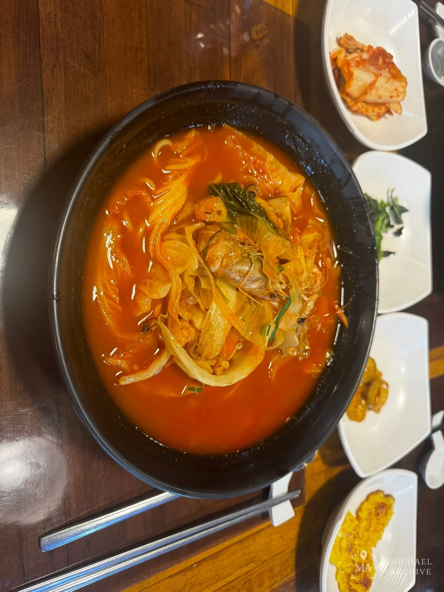 붉은 국물의 짬뽕 한 그릇. 옆에 김치와 나물 반찬이 흰 접시에 담겨 나왔다.