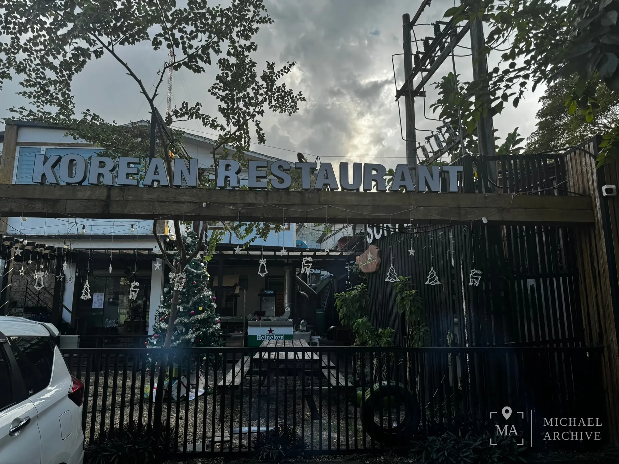검은 철제 담장 위에 「KOREAN RESTAURANT」라고 적힌 간판이 걸려 있다. 안쪽에 나무와 조명이 보인다.