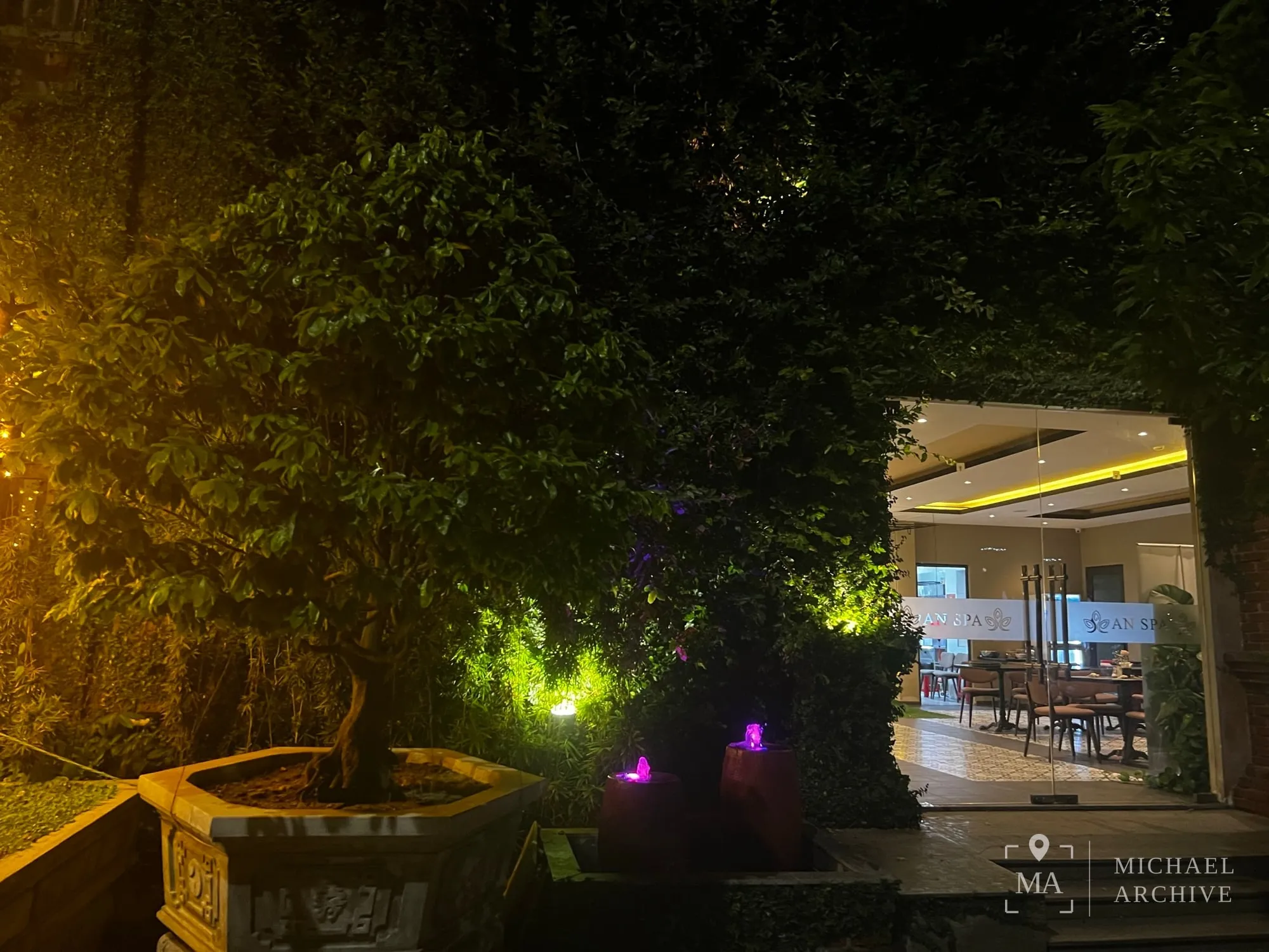 밤의 정원, 조명을 받은 나무와 분수, 유리벽 너머로 보이는 AN SPA 실내