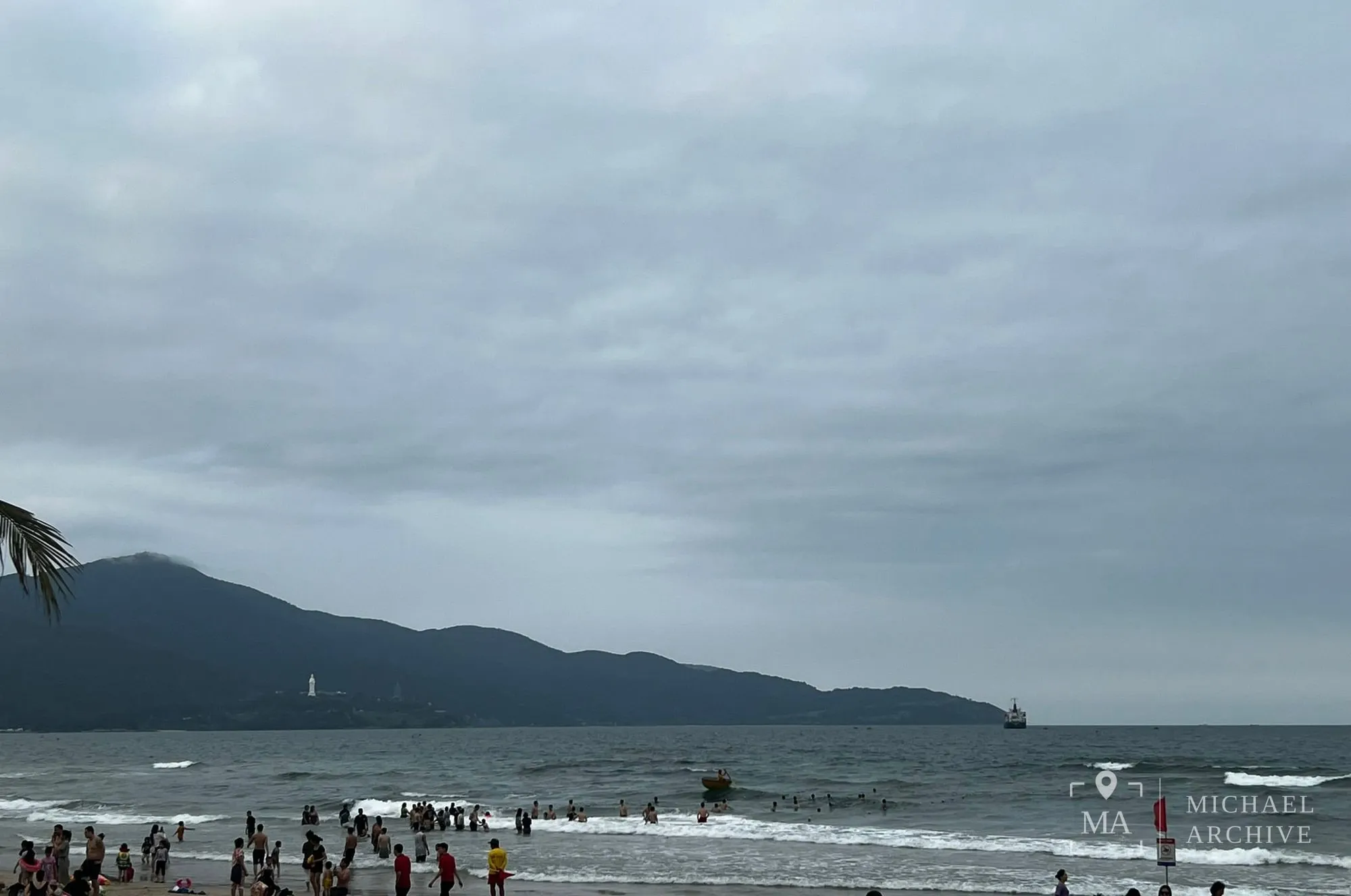 바다 건너 선짜반도 능선, 파도 앞에 붉은 깃발과 안내판이 서 있다