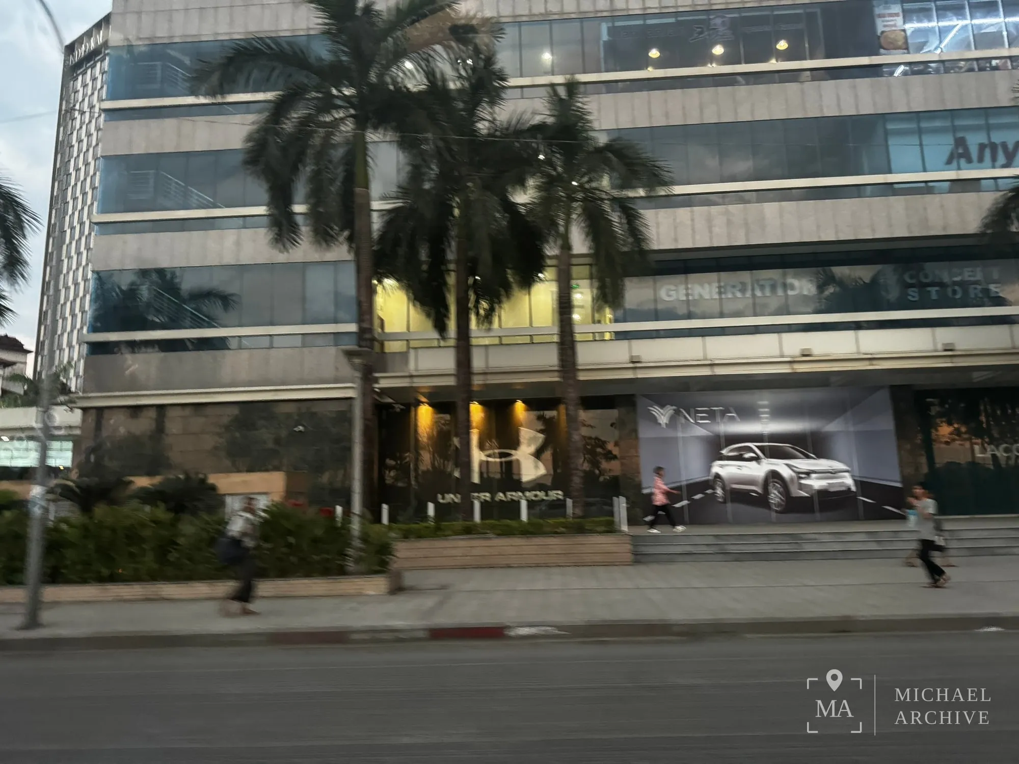 도로변 상가 건물. 1층에 Under Armour 매장이 있고 앞에 야자수가 서 있다.