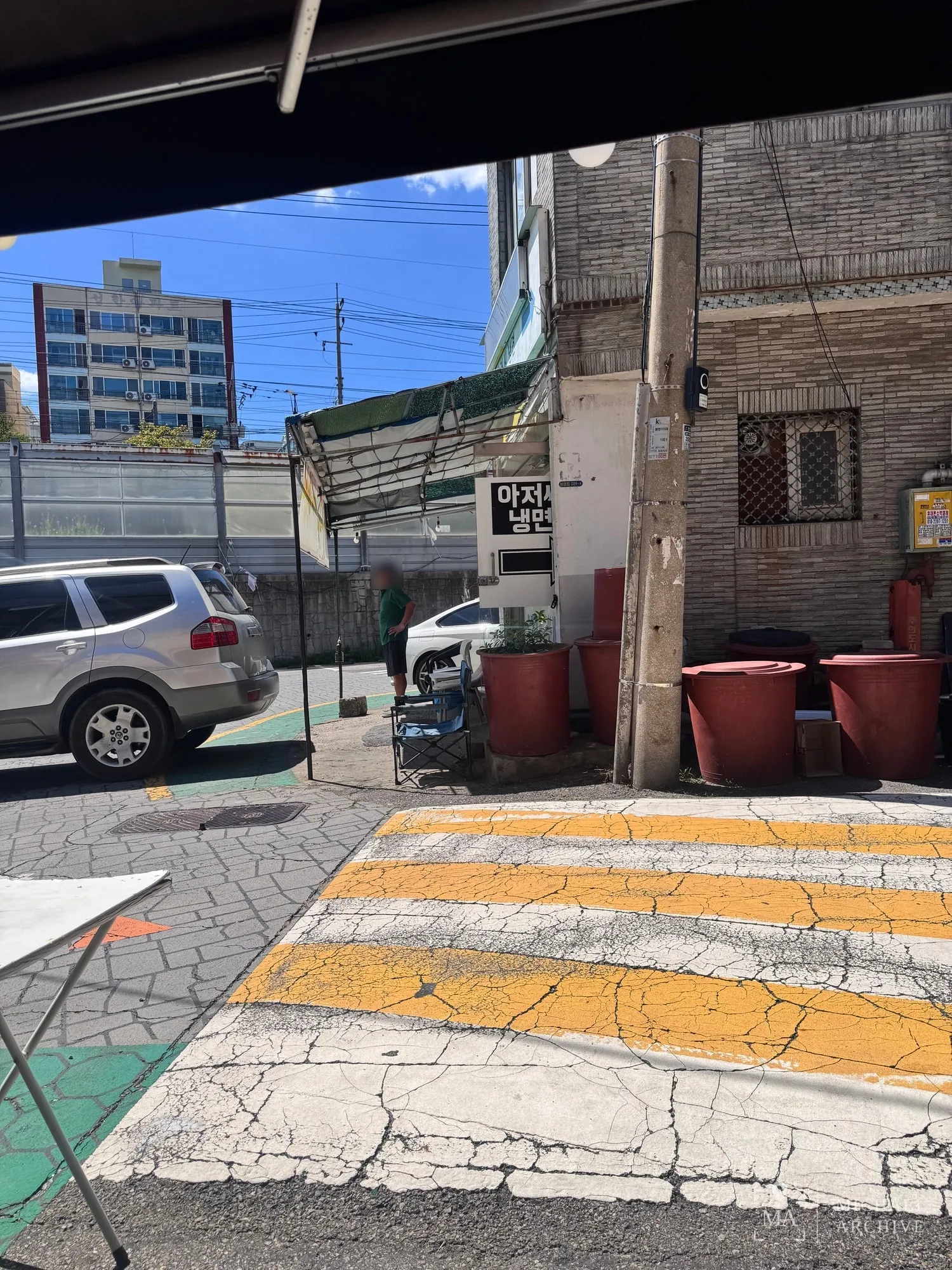 가게에서 본 바깥 — 횡단보도 건너 「아저씨 냉면」 간판과 붉은 고무 대야들